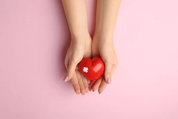 Жіночі руки з червоним серцем на кольоровому фоні. Концепція кардіології — стокове фото