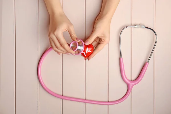 Female hands with red heart and stethoscope on white wooden background. Cardiology concept — Stock Photo, Image