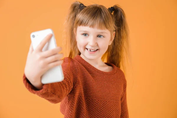 Little girl taking selfie on color background — Stock Photo, Image