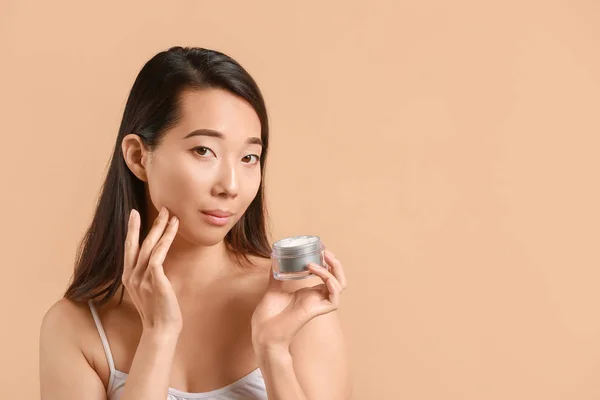 Mooie jonge Aziatische vrouw met crème op kleur achtergrond — Stockfoto