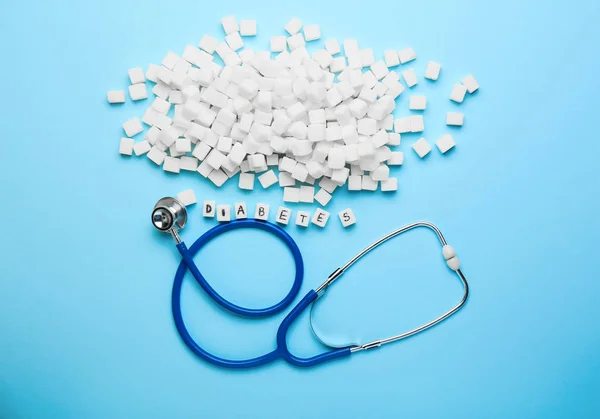 Stethoscope, sugar and word DIABETES on color background — Stock Photo, Image