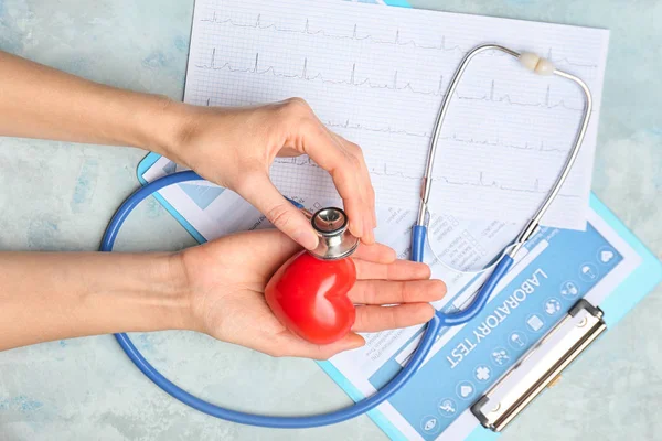 Kırmızı kalpli kadın eller, steteskop, kardiyogram ve ışık arkaplan üzerinde laboratuvar testi — Stok fotoğraf
