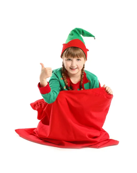 Menino elfo sentado no saco de Papai Noel e mostrando gesto de polegar para cima no fundo branco — Fotografia de Stock