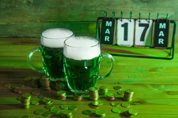 Mugs of green beer for St. Patrick's Day and coins on wooden table