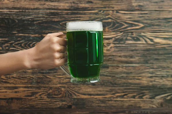Female hand with mug of green beer for St. Patrick's Day on wooden background — Stock Photo, Image