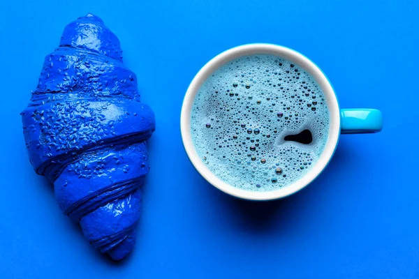 Niebieski rogalik i filiżanka kawy na tle koloru — Zdjęcie stockowe