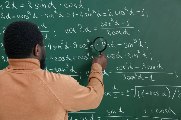 Profesor de matemáticas afroamericano con lupa cerca de pizarra en el aula — Foto de Stock