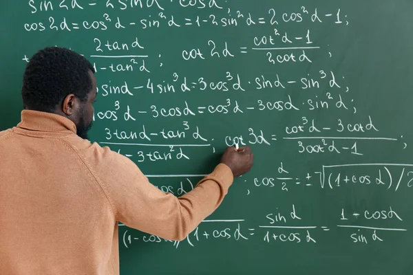 Profesor de matemáticas afroamericano escribiendo en pizarra en el aula — Foto de Stock