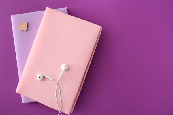 Books and modern earphones on color background. Concept of audiobook