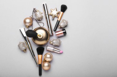 Makyaj malzemeli bir şişe parfüm ve gri arka planda Noel dekoru.