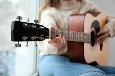 Gitarlı genç kadın pencerenin pervazında oturuyor.
