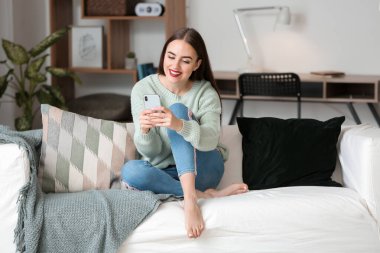 Evinde cep telefonu olan güzel genç bir kadın.