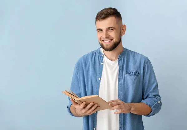 Handsome young man reading book on color background — Stock Photo, Image