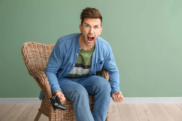 Angry man playing video games while sitting in armchair near color wall — Stockfoto