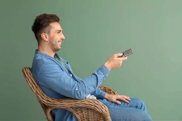 Handsome man watching TV while sitting in armchair on color background — Stock Photo, Image