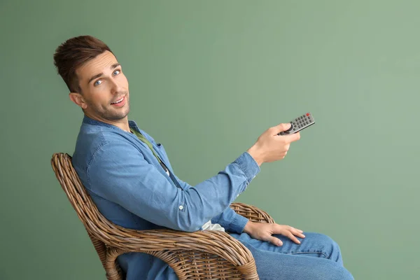 ハンサムな男見てテレビながら座っていますでアームチェア上の色の背景 — ストック写真