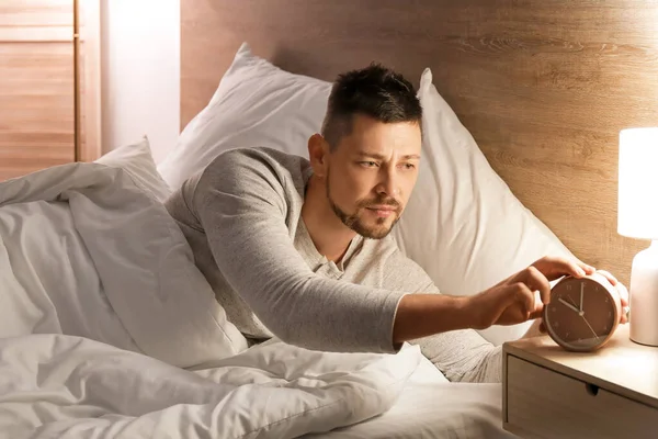 Handsome man setting an alarm while lying in bed at night — Stockfoto