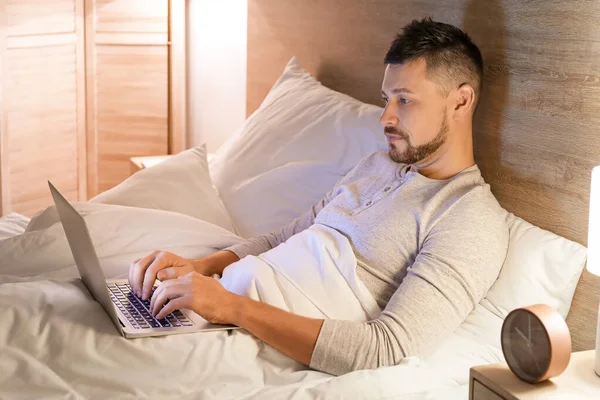 Mężczyzna z laptopem w łóżku w nocy — Zdjęcie stockowe