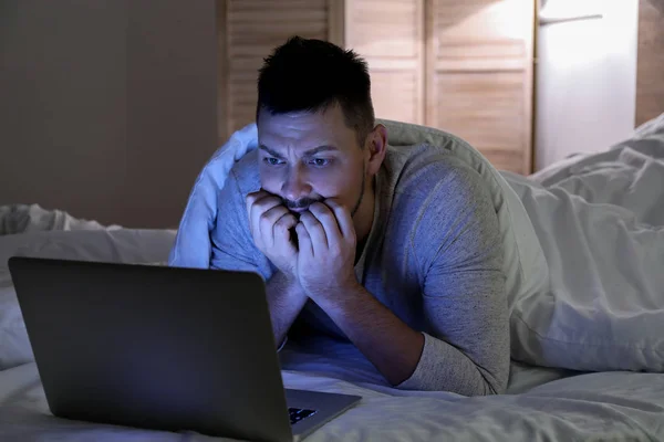 Emotional man with laptop in bed at night — Stockfoto