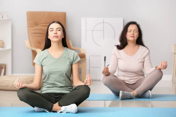 Mulher madura e sua filha adulta meditando juntos em casa — Fotografia de Stock