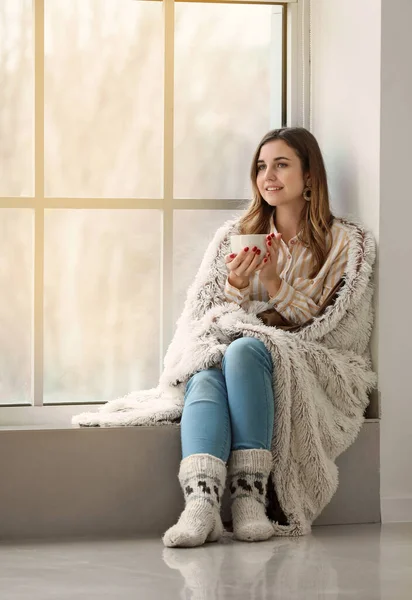 Young woman drinking hot tea on window sill at home — Stock Photo, Image