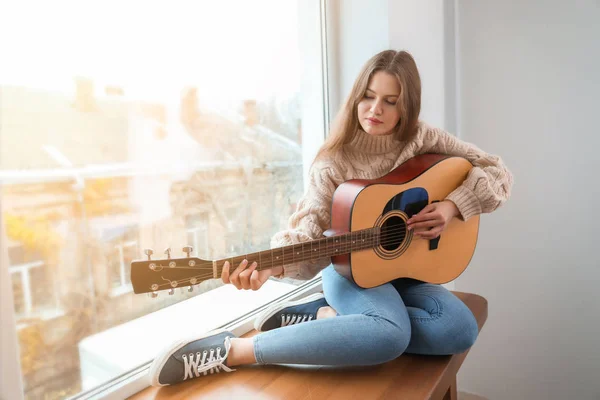 Young woman with guitar sitting on window sill at home — Stock Photo, Image