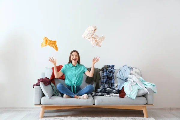 Jovem com montão de roupas no sofá dentro de casa — Fotografia de Stock