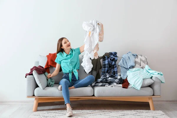 Jovem com montão de roupas no sofá dentro de casa — Fotografia de Stock