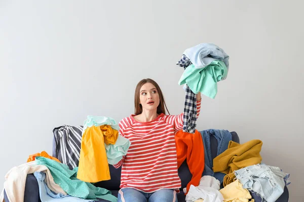 Troubled woman with heap of clothes on sofa indoors