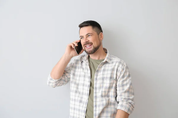Mature man talking by phone on light background — Stock Photo, Image