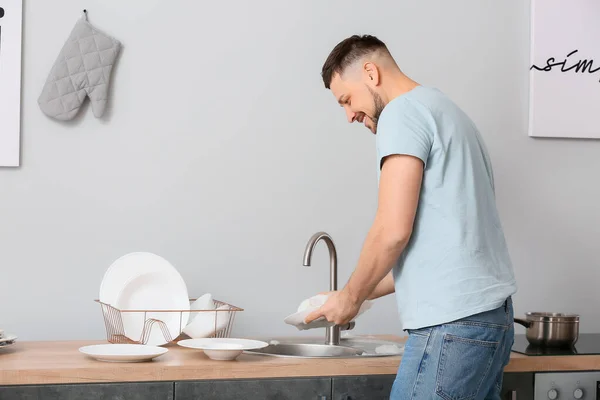 Handsome man washing dishes in kitchen — Stock Photo, Image