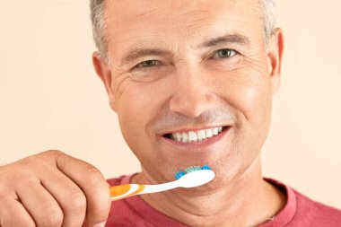 Renkli arka planda dişlerini fırçalayan olgun bir adam