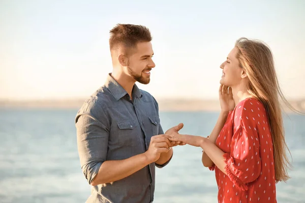 Young man putting ring on finger of his fiancee after marriage proposal near river — Stock Photo, Image