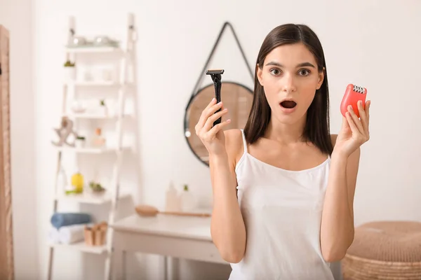 Surprised young woman with razor and epilator in bathroom — Stock Photo, Image