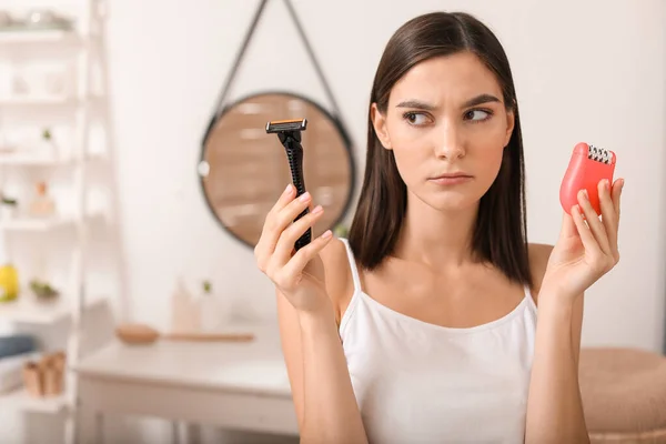 Thoughtful young woman with razor and epilator in bathroom