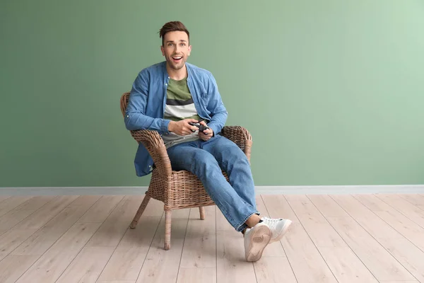 Hombre guapo jugando videojuegos mientras está sentado en un sillón cerca de la pared de color — Foto de Stock