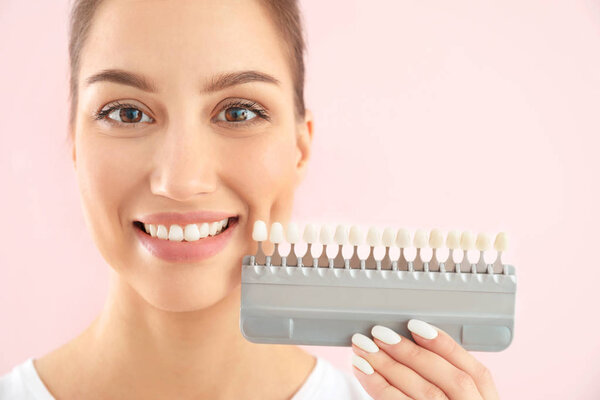 Beautiful young woman with teeth color samples on color background