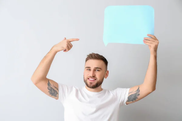 Young man with blank speech bubble on light background — Stock Photo, Image