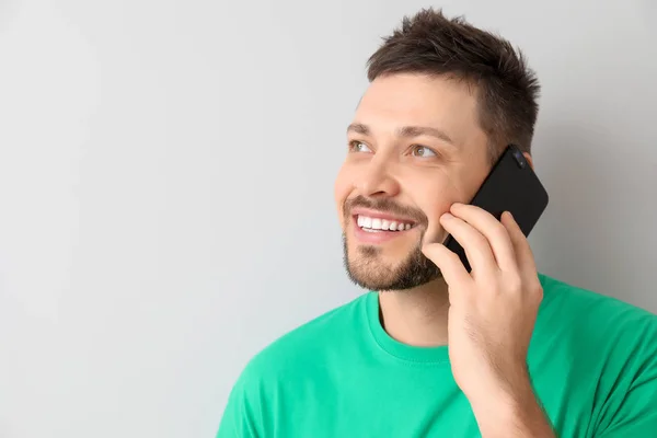 Happy man talking by mobile phone on light background — Stock Photo, Image