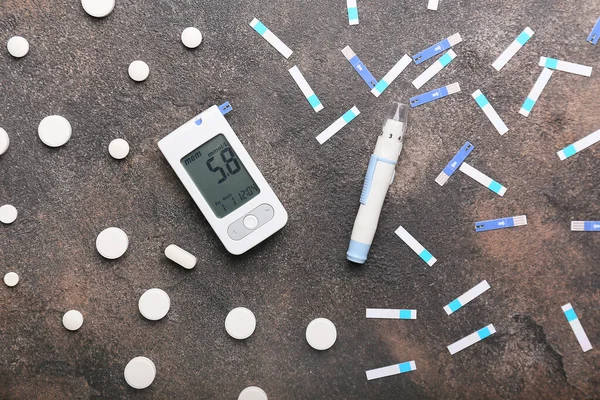 Таблетки, глюкометр і ланцетна ручка на сірому фоні. Концепція діабету — стокове фото