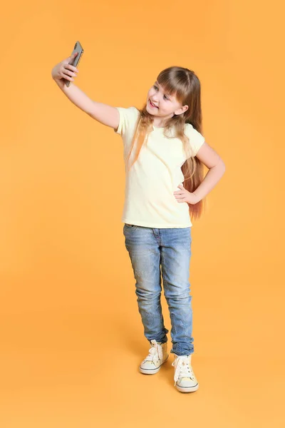 Cute little girl taking selfie on color background — Stock Photo, Image