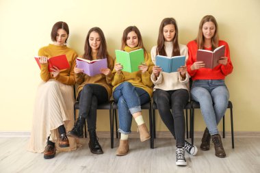 Kitapları olan genç kadınlar renk duvarının yanında oturuyor.