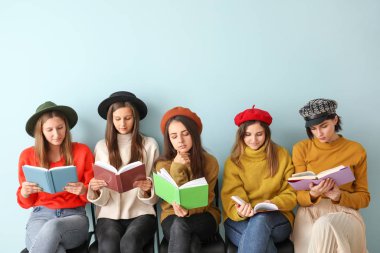 Kitapları olan genç kadınlar renk duvarının yanında oturuyor.