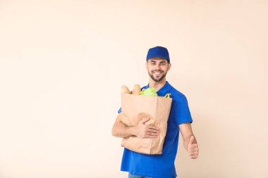 Handsome worker of food delivery service showing thumb-up on color background
