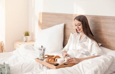 Güzel genç bir bayanın yatakta kahvaltı ettiği bir sabah.