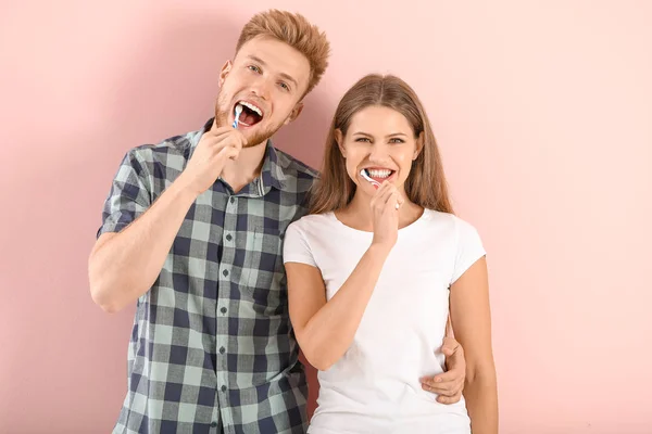 Young couple brushing teeth on color background — Stock Photo, Image