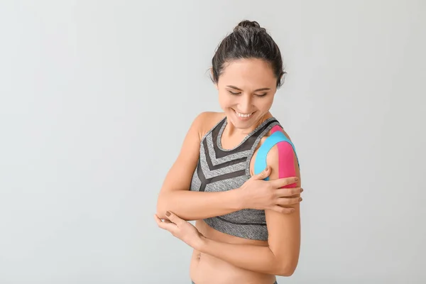 Sportieve vrouw met fysioband aangebracht op schouder tegen lichte achtergrond — Stockfoto
