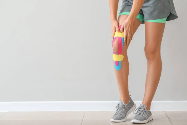 Mulher esportiva com fita fisiográfica aplicada no joelho contra fundo claro — Fotografia de Stock
