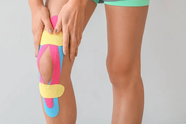 Donna sportiva con nastro fisioterapico applicato sul ginocchio su sfondo chiaro, primo piano — Foto Stock