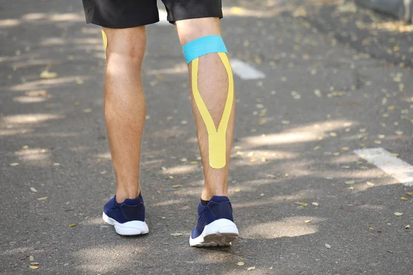 Fizyoterapi bandı olan sportif bir adam açık havada bacağa uygulanmış.